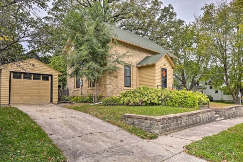 A charming yellow house with a green roof, surrounded by trees and a well-maintained garden, with a garage nearby.