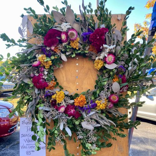A vibrant floral wreath made of colorful flowers and greenery displayed on a wooden board.