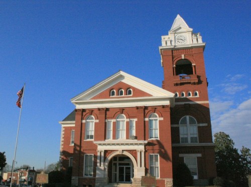 Historic red brick courthouse with a clock tower, blue sky, and an American flag in front.