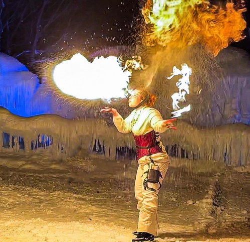 A performer breathes fire, creating a large flame against a snowy backdrop, showcasing a dramatic fire display.