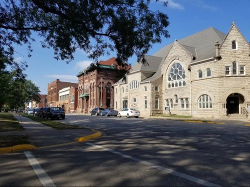 A street view featuring historic buildings, including a stone church and brick structures, under a clear blue sky.