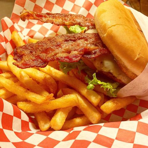 A delicious burger with bacon and lettuce, served with a side of golden French fries in a red-checkered basket.