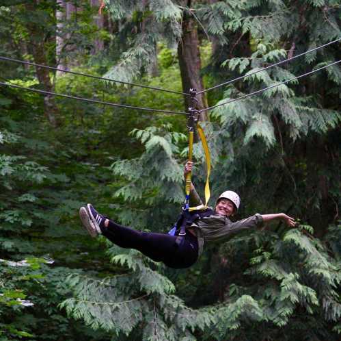 A person zip-lining through a lush green forest, wearing a helmet and harness, with arms outstretched in excitement.