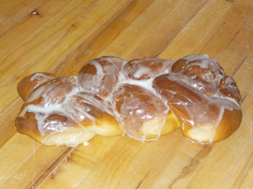 A glazed, braided sweet bread resting on a wooden surface.