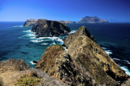 A scenic coastal view featuring rugged cliffs and clear blue waters under a bright sky.