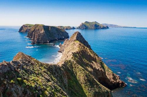 A scenic view of rugged coastal cliffs and islands against a clear blue ocean and sky.