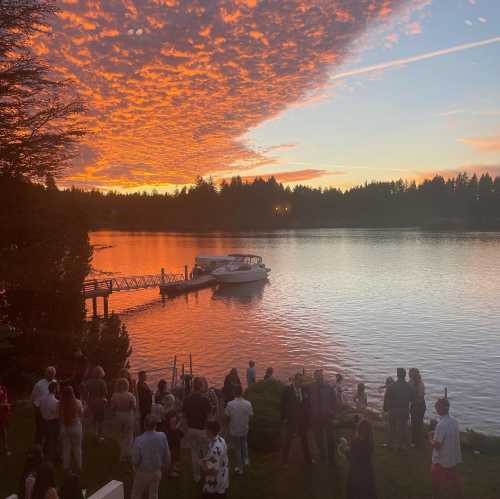 A vibrant sunset over a lake, with people gathered near a dock and a boat on the water.