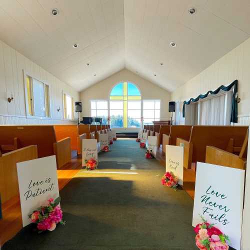 A wedding venue with wooden pews, floral decorations, and signs displaying "Love is Patient" and "Love Never Fails."