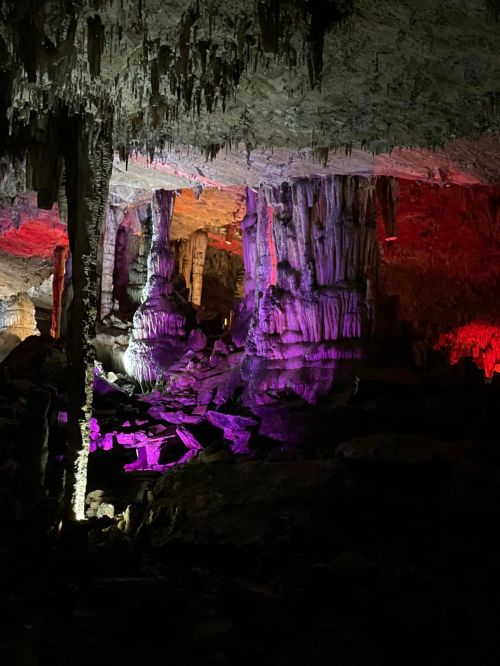 Colorful stalactites and stalagmites illuminated in a cave, showcasing intricate rock formations and dramatic lighting.