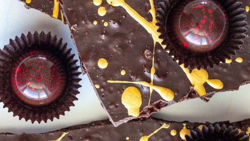 Close-up of dark chocolate with vibrant yellow and red splashes, featuring decorative chocolate cups.