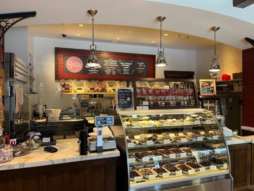 A cozy café counter displaying a variety of pastries and desserts, with a menu board above and a coffee machine on the side.