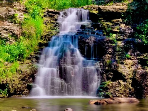 A serene waterfall cascading over rocky cliffs, surrounded by lush greenery and reflecting in a calm pool below.