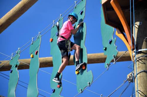 A child in a pink shirt climbs a colorful rock wall against a clear blue sky.