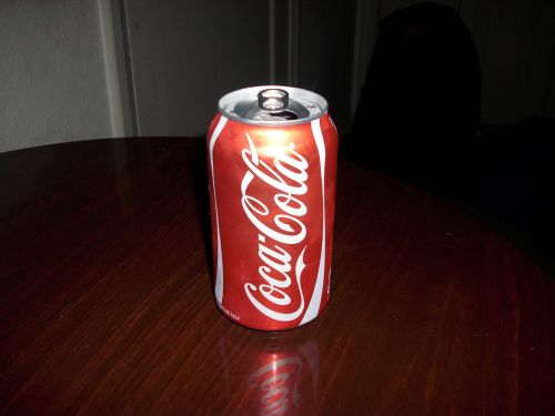 A can of Coca-Cola sits on a wooden table in a dimly lit room.