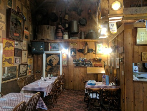 Cozy restaurant interior with wooden walls, checkered tablecloths, and vintage decor, including posters and memorabilia.