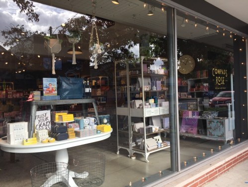 A storefront display featuring various colorful products, including books, gifts, and home decor, with warm lighting.