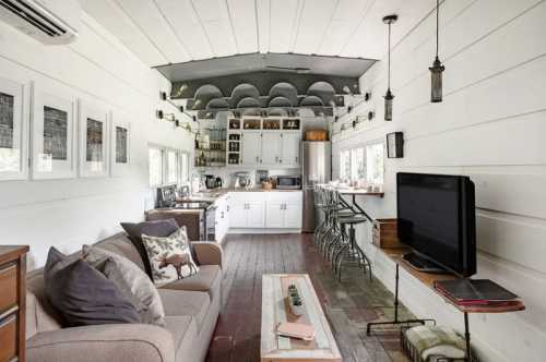 Cozy interior of a modern tiny home featuring a living area, kitchen, and bar seating with white walls and wooden floors.