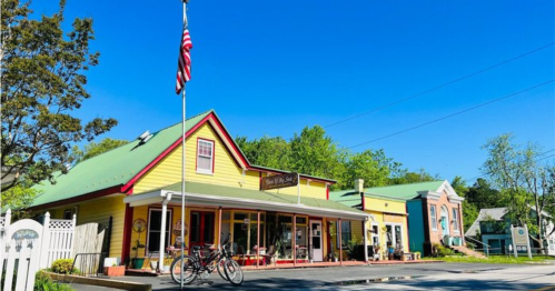 A colorful yellow building with a green roof, featuring a shop front and an American flag, set against a clear blue sky.