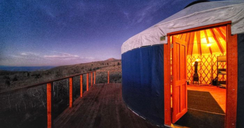 A cozy yurt with an open door, set against a twilight landscape and mountains in the background.