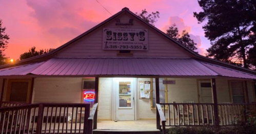 A cozy restaurant named "Sissy's" with a pink sunset in the background and a welcoming neon sign.