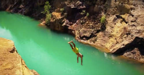 A person diving into a vibrant turquoise river surrounded by rocky cliffs and greenery.