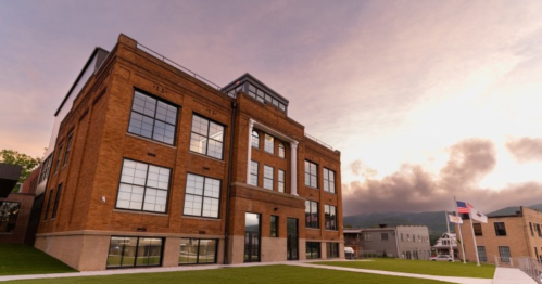 Historic brick building with large windows, set against a cloudy sky and green lawn.