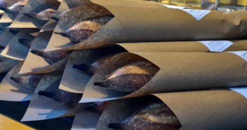 A stack of freshly baked baguettes wrapped in brown paper, neatly arranged on a table.