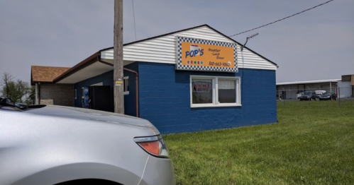 A blue building with a sign reading "Pop's Restaurant & Lounge" next to a parked silver car on a grassy area.