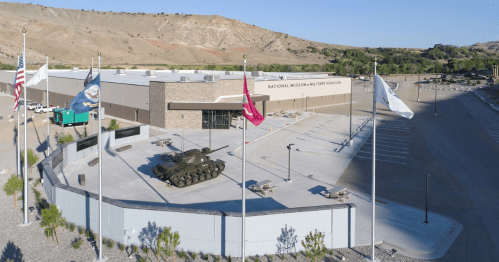 Aerial view of the National Museum of Military Vehicles, featuring a tank and flags in front of a modern building.