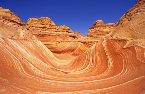 Colorful, swirling sandstone formations under a clear blue sky, showcasing natural erosion patterns in a desert landscape.
