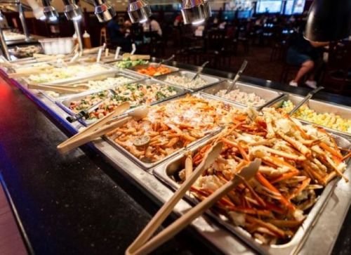 A buffet with various colorful dishes, including salads and vegetables, displayed in metal trays with serving utensils.