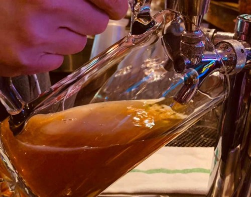 A hand pours beer from a tap into a glass, with foam rising at the top.