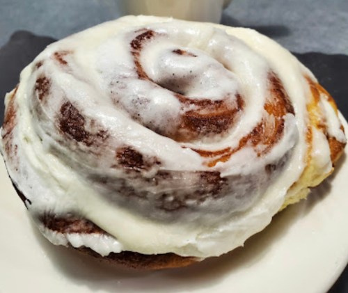 A close-up of a frosted cinnamon roll on a plate, showcasing its swirled layers and creamy icing.