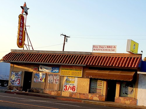 A roadside building with a liquor store sign and a BBQ restaurant, featuring colorful banners and a retro star sign.