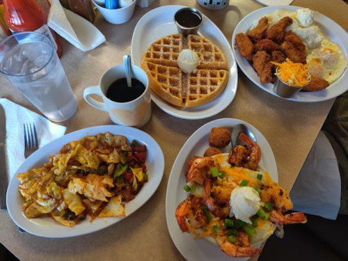 A table spread with waffles, fried chicken, shrimp, cabbage stir-fry, and coffee, showcasing a hearty meal.