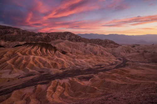 A stunning desert landscape at sunset, featuring layered hills and vibrant pink and orange skies.