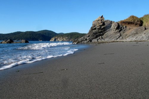 A serene beach scene with gentle waves lapping at the shore, rocky formations, and lush green hills in the background.