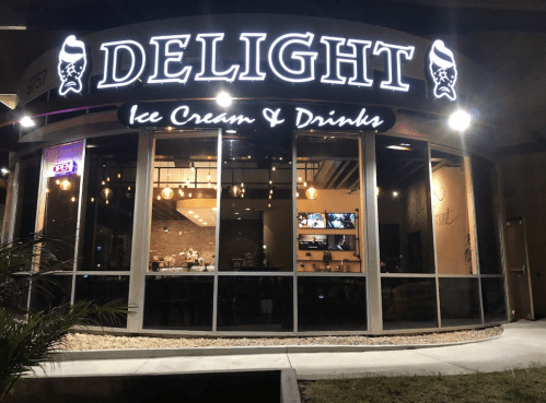 Exterior of "Delight" ice cream and drinks shop, featuring large illuminated sign and glass windows at night.