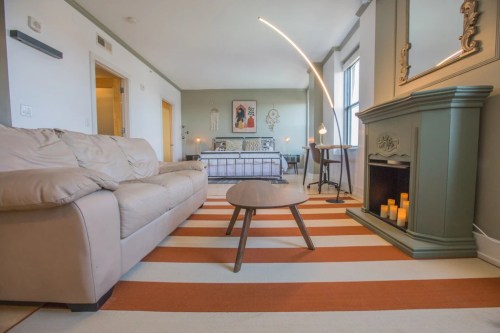Cozy living space featuring a beige sofa, round coffee table, striped rug, and a decorative fireplace.