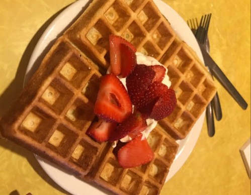 A plate of golden waffles topped with whipped cream and fresh strawberries, set on a yellow table.