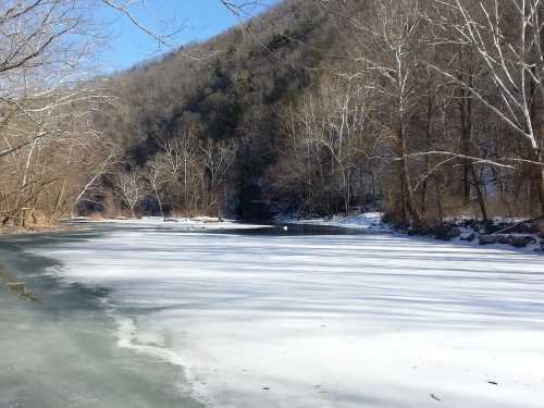 A serene winter landscape featuring a frozen river surrounded by bare trees and a snow-covered hillside.