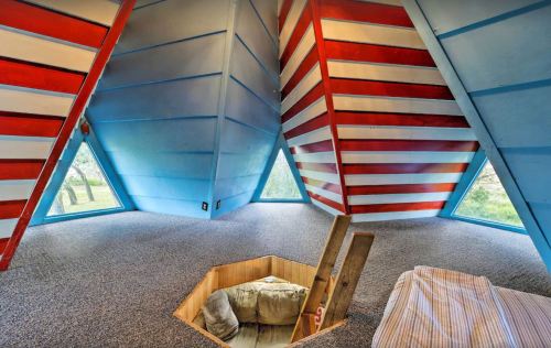 Interior of a unique, colorful room with slanted walls, large windows, and a cozy seating area in the center.