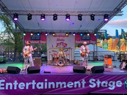 A band performs on an outdoor stage with colorful lights and a banner reading "Entertainment Stage."