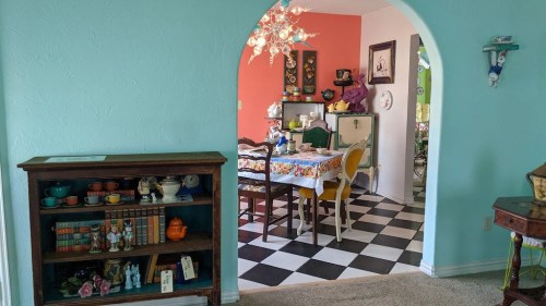 A colorful dining area with a patterned tablecloth, surrounded by vintage decor and a turquoise wall.