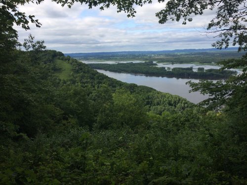 A scenic view of a river winding through lush green hills under a cloudy sky.