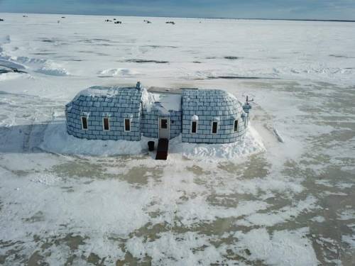 A snow-covered igloo-like structure stands on a vast, icy landscape under a clear sky.