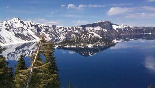 A scenic view of a snow-capped mountain range reflecting in a calm blue lake under a clear sky.