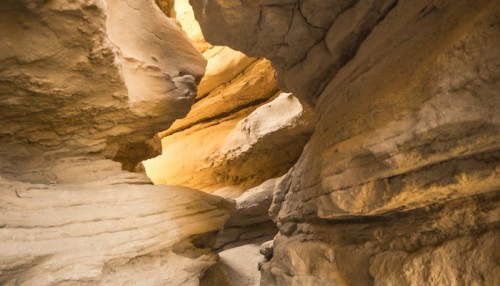 Narrow canyon with layered rock formations and warm light illuminating the path ahead.