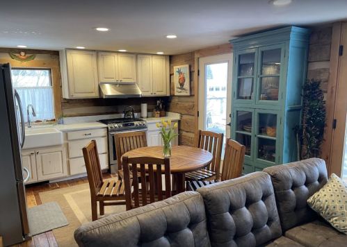 Cozy kitchen with wooden cabinets, a round dining table, and a blue cabinet, featuring natural light and a comfortable sofa.