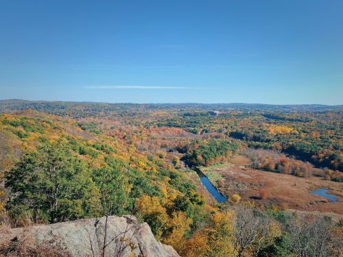 A scenic view of a colorful autumn landscape with rolling hills, a winding river, and clear blue skies.